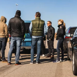 Grupp människor som står och samtalar bredvid bilar.