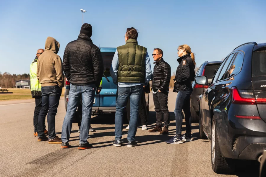 Grupp människor som står och samtalar bredvid bilar.