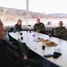 Personer som sitter runt ett bord i ett konferensrum med stora fönster ut mot en halkbana